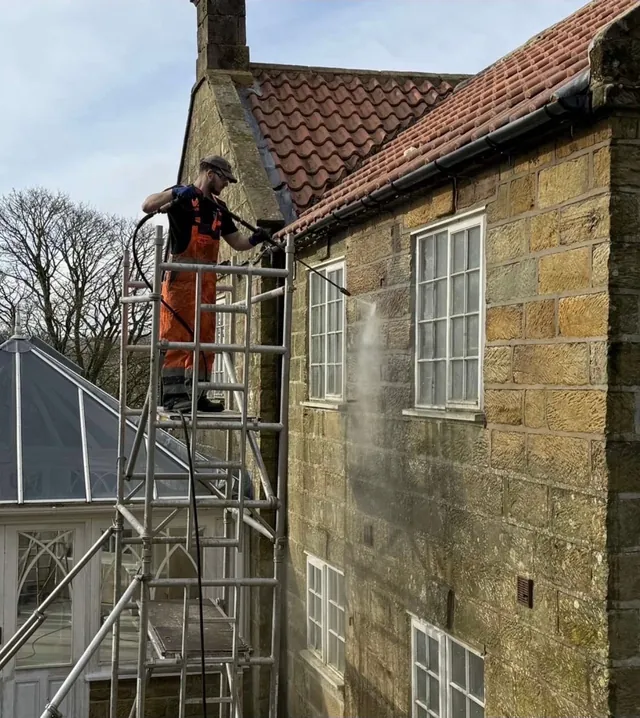 Roof cleaning from a scaffold tower beside a stone house